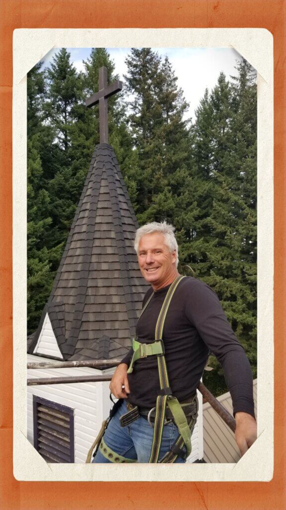 A photo of founder, Terry Slate, in a safety harness next to a church steeple he roofed.
